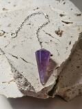 Faceted Amethyst pendulum on a silver chain, lying on a pale stone slab