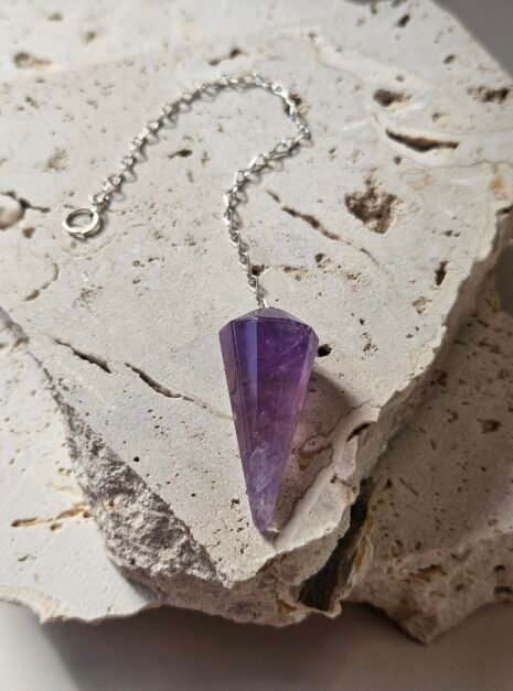 Faceted Amethyst pendulum on a silver chain, lying on a pale stone slab
