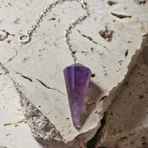 Faceted Amethyst pendulum on a silver chain, lying on a pale stone slab
