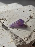 Faceted Amethyst pendulum and silver chain on a stone slab, seen from another angle