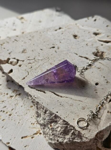 Amethyst Pendulum 2 Faceted Amethyst pendulum and silver chain on a stone slab, seen from another angle