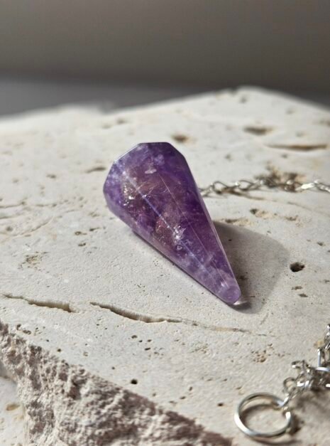 Amethyst Pendulum 3 Faceted Amethyst pendulum on a stone slab, showing the cut facets