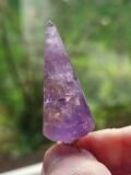 Faceted Amethyst pendulum held up to the light, showing the purple through the stone