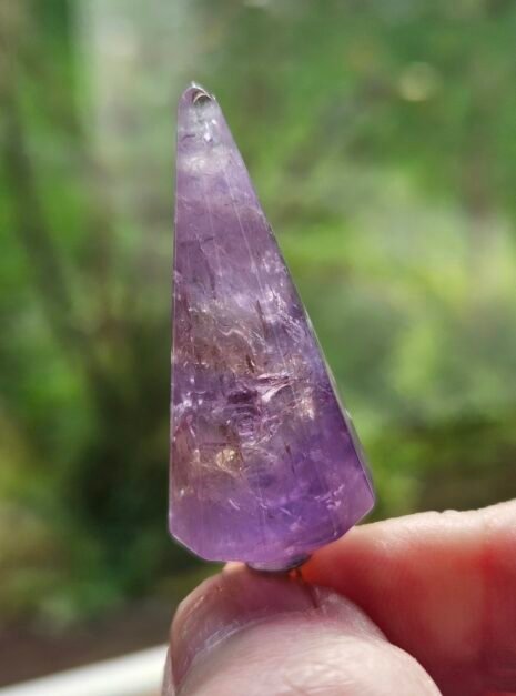 Amethyst Pendulum 5 Faceted Amethyst pendulum held up to the light, showing the purple through the stone