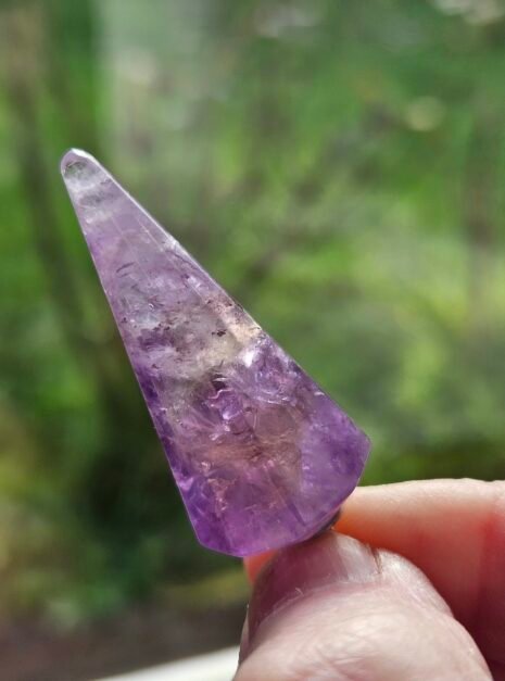 Amethyst Pendulum 6 Faceted Amethyst pendulum held to the light, showing the facets catching the light