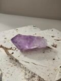 Rough Amethyst point on a pale stone slab, rotated to another angle