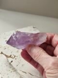 Rough Amethyst point held in the hand above a pale stone slab