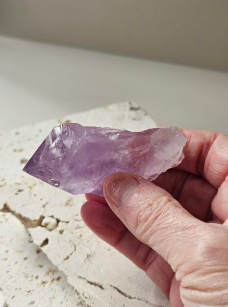 Amethyst Rough Point 3 Rough Amethyst point held in the hand above a pale stone slab