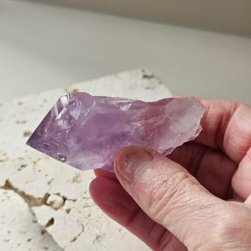 Rough Amethyst point held in the hand above a pale stone slab