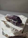 Bahia Amethyst point lying at an angle on a pale stone slab, banded purple running up the crystal
