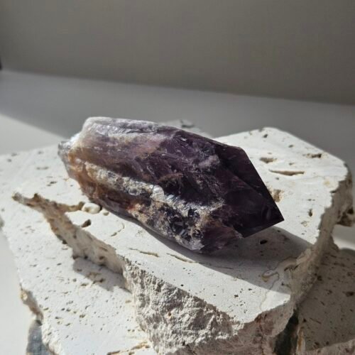 Bahia Amethyst point lying at an angle on a pale stone slab, banded purple running up the crystal