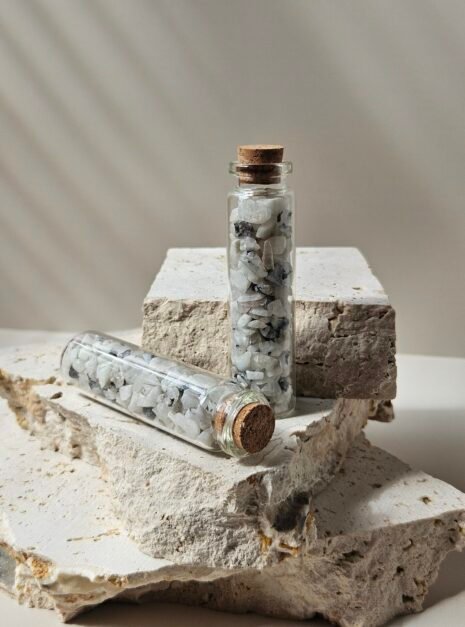 Moonstone Vials 1 One vial of Rainbow Moonstone chips standing on a stone, a second lying on its side in front