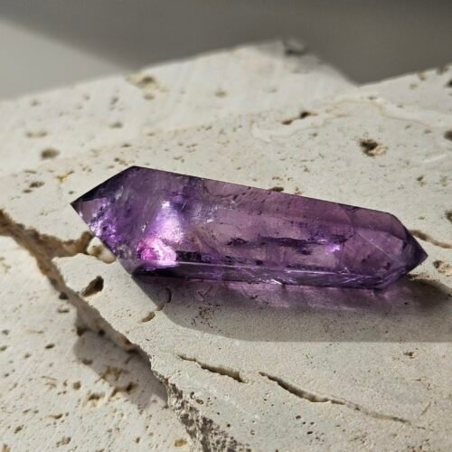 Double-terminated Amethyst wand in sunlight, a pink and white glint visible through the crystal