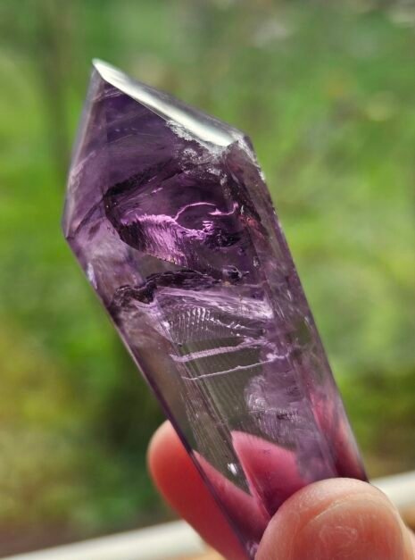 amethyst wand 7 Double-terminated Amethyst wand held up to the light, pink glow through the crystal