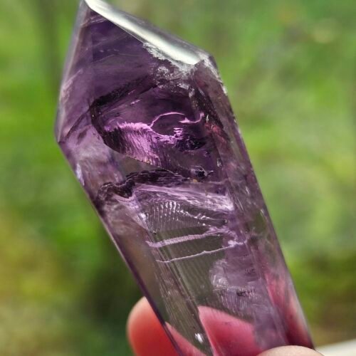 amethyst wand 7 Double-terminated Amethyst wand held up to the light, pink glow through the crystal
